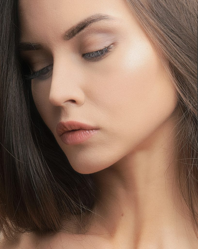 Close-up studio portrait of a woman showcasing elegant beauty with soft nude makeup and clear skin.